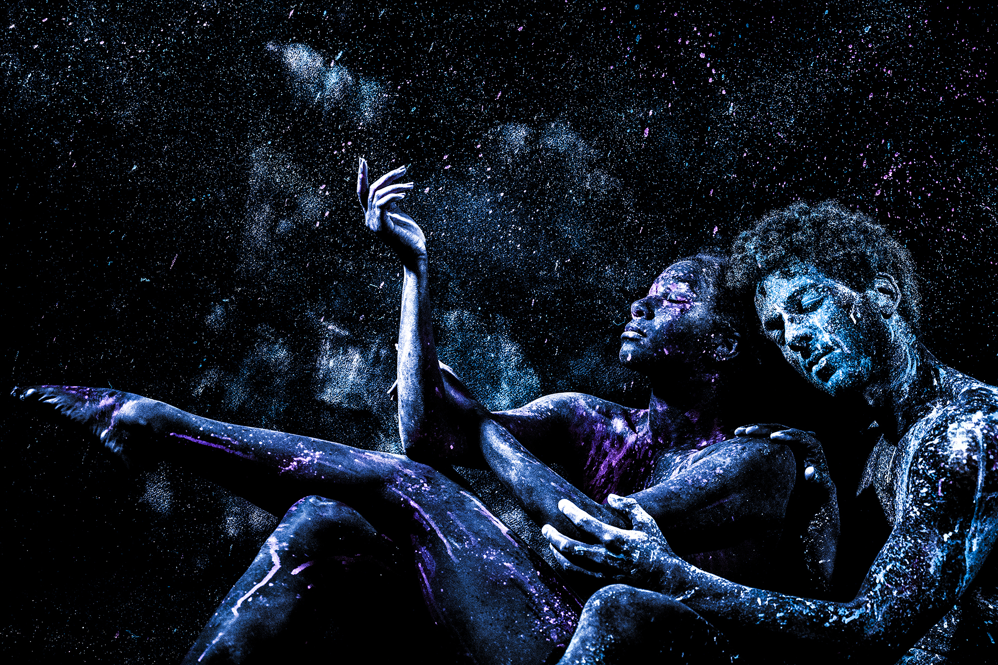 Two black- and blue-hued African American figures cradle each other against stars in the dark sky.