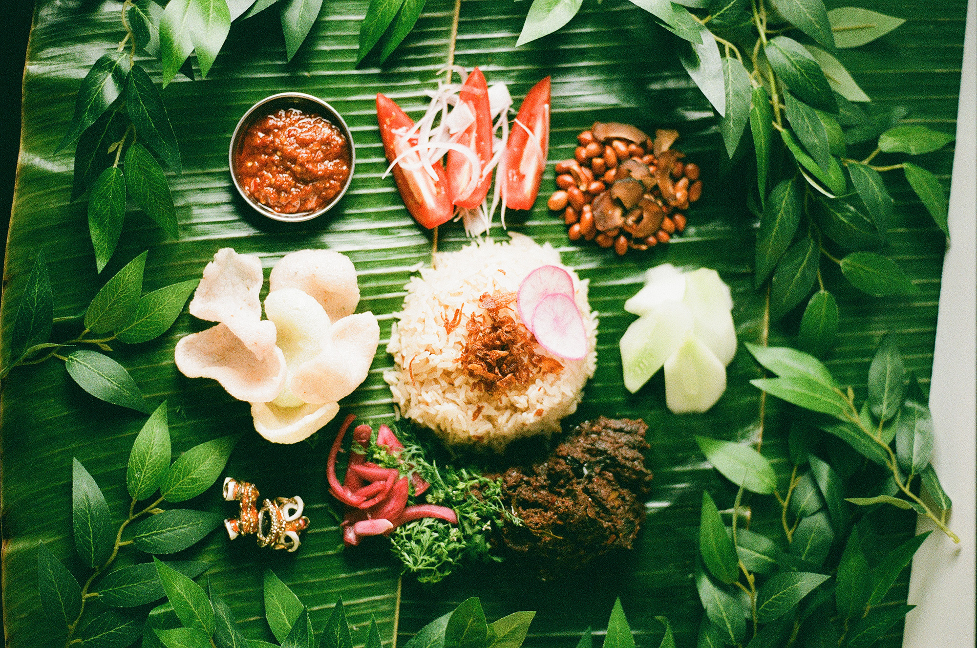 Rice, peanuts, sambal and assorted vegetables, served on pandan leaves.