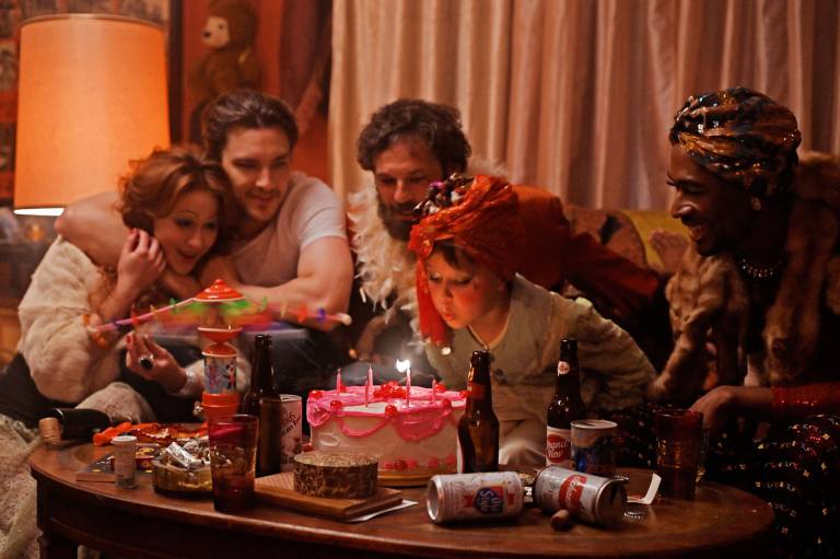 adults cheer on child blowing out candles on cake