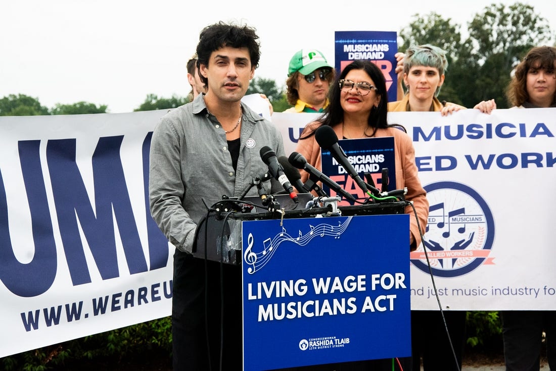 A musician speaks at a podium next to a congresswoman.