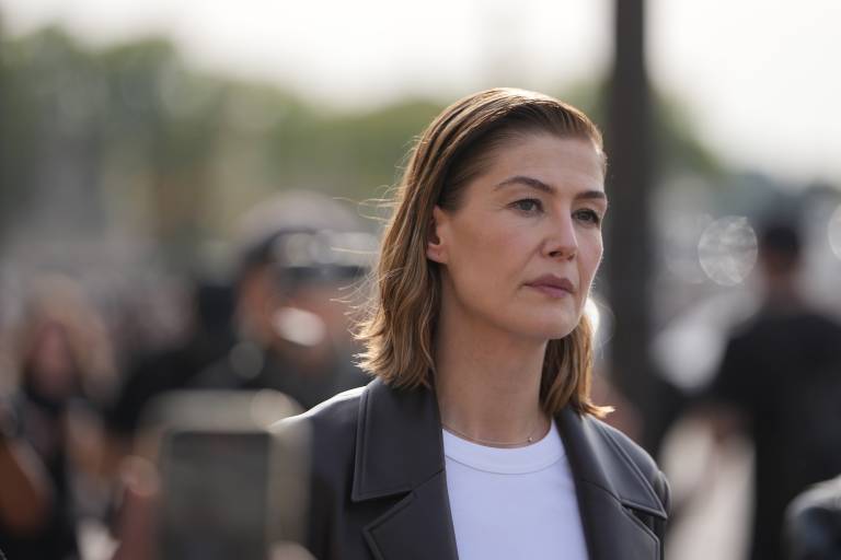 A white, attractive middle-aged woman wearing a white t-shirt and black leather jacket looks ahead blankly.