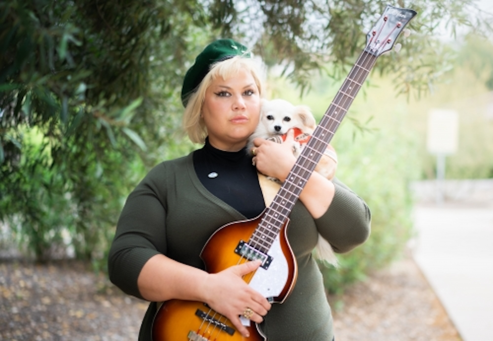 A person wearing a hat, holding a guitar in one hand and a dog in the other.