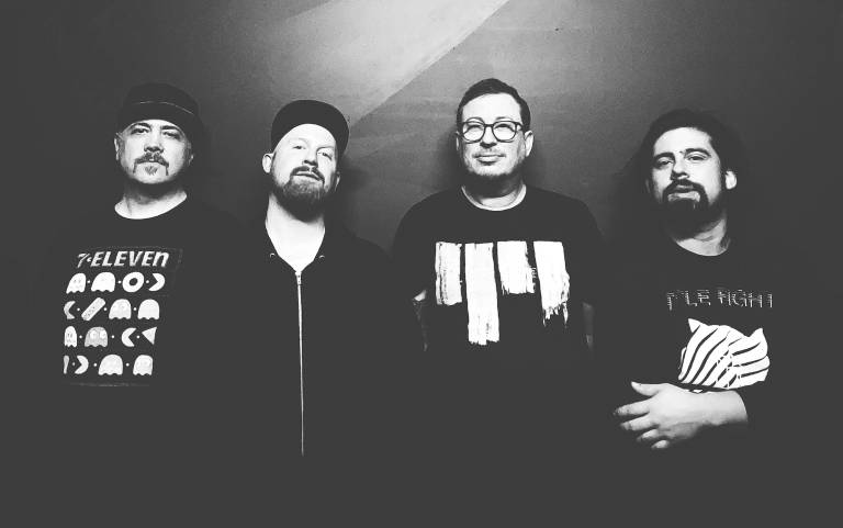 A black and white photo of four men wearing black clothes lining up against a dark backdrop.
