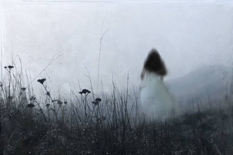 An out of focus, bluurred ghostly woman wearing a white dress, running away from the camera. On a misty winters day in the countryside. With an artistic, textured, edit.