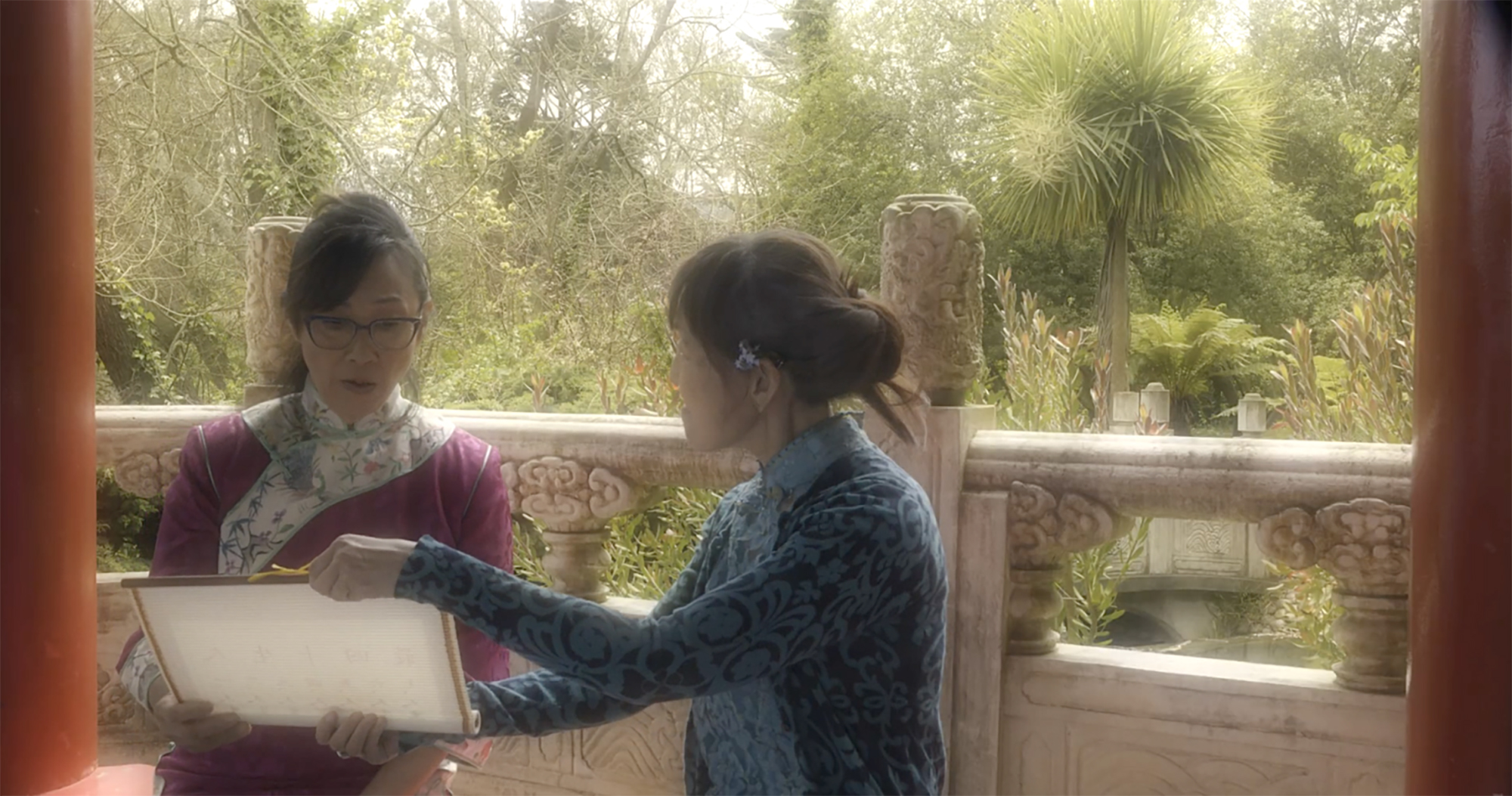 A blurry movie scene shows two characters talking, one holding an unfurled scroll.