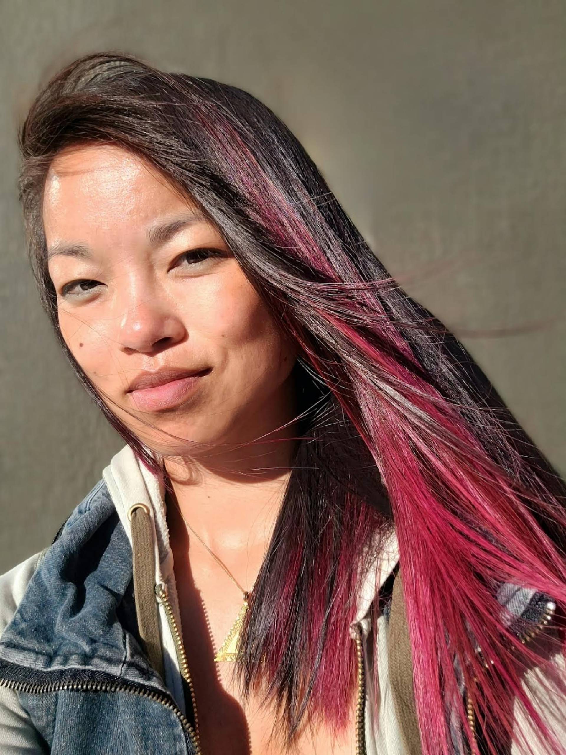 A Chinese-American woman with dyed red hair and a hooded sweater poses for a photo. 