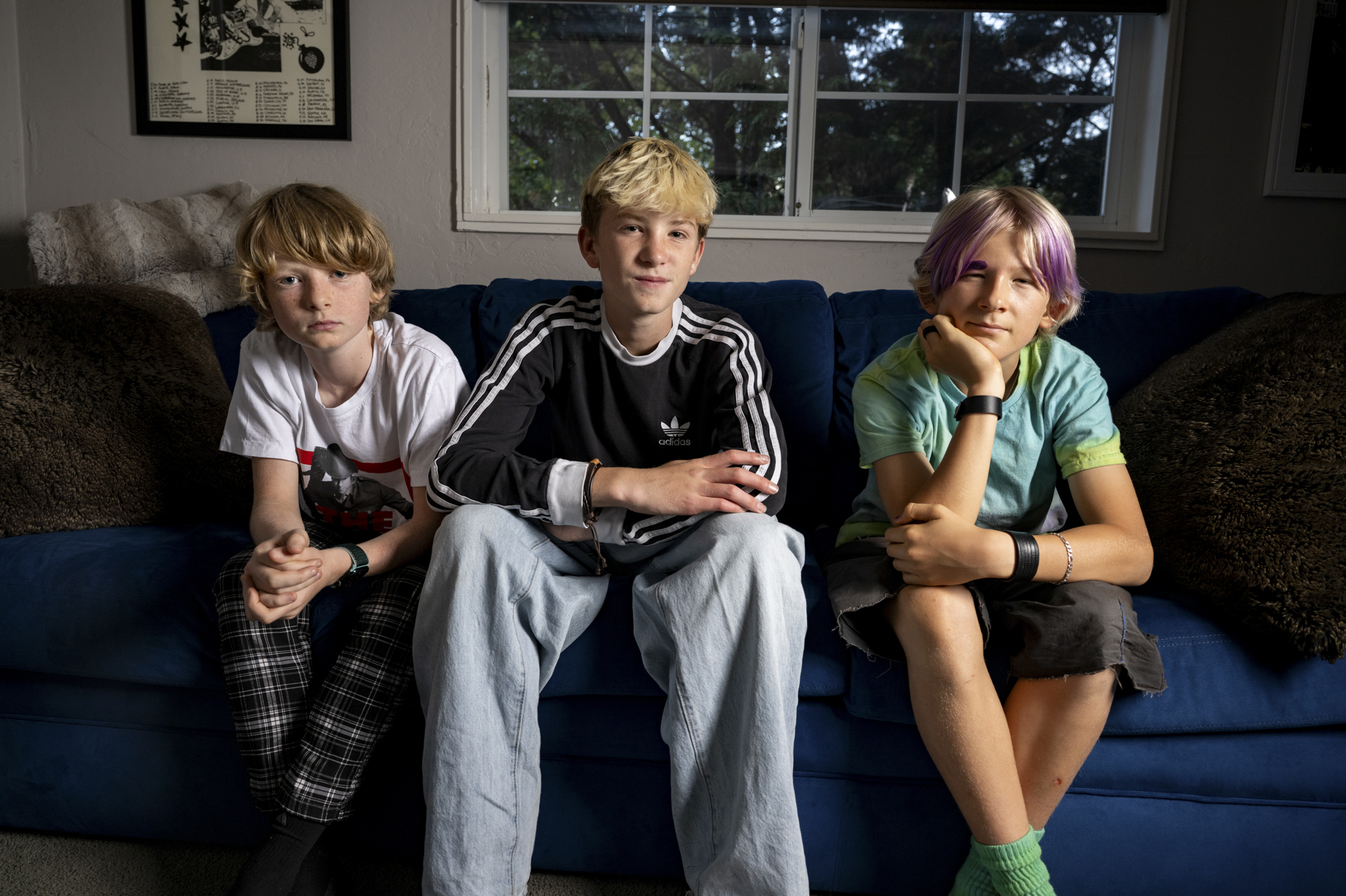 Three young musicians sit on the couch and look into the camera.