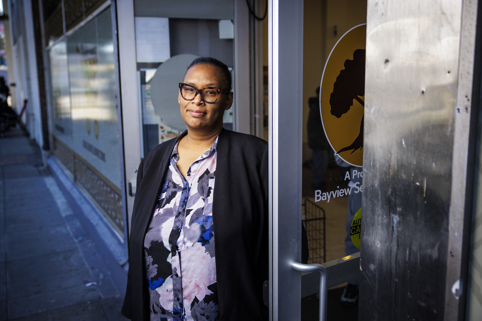 A Black woman poses for a portrait while standing outside the doorway of a storefront.