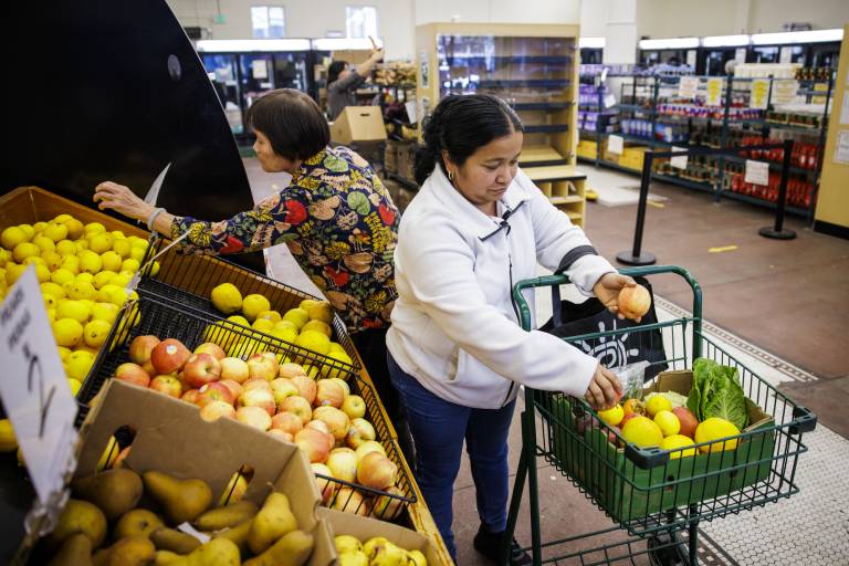 Woman in a grocery store loading fresh produce intp her shopping cart.