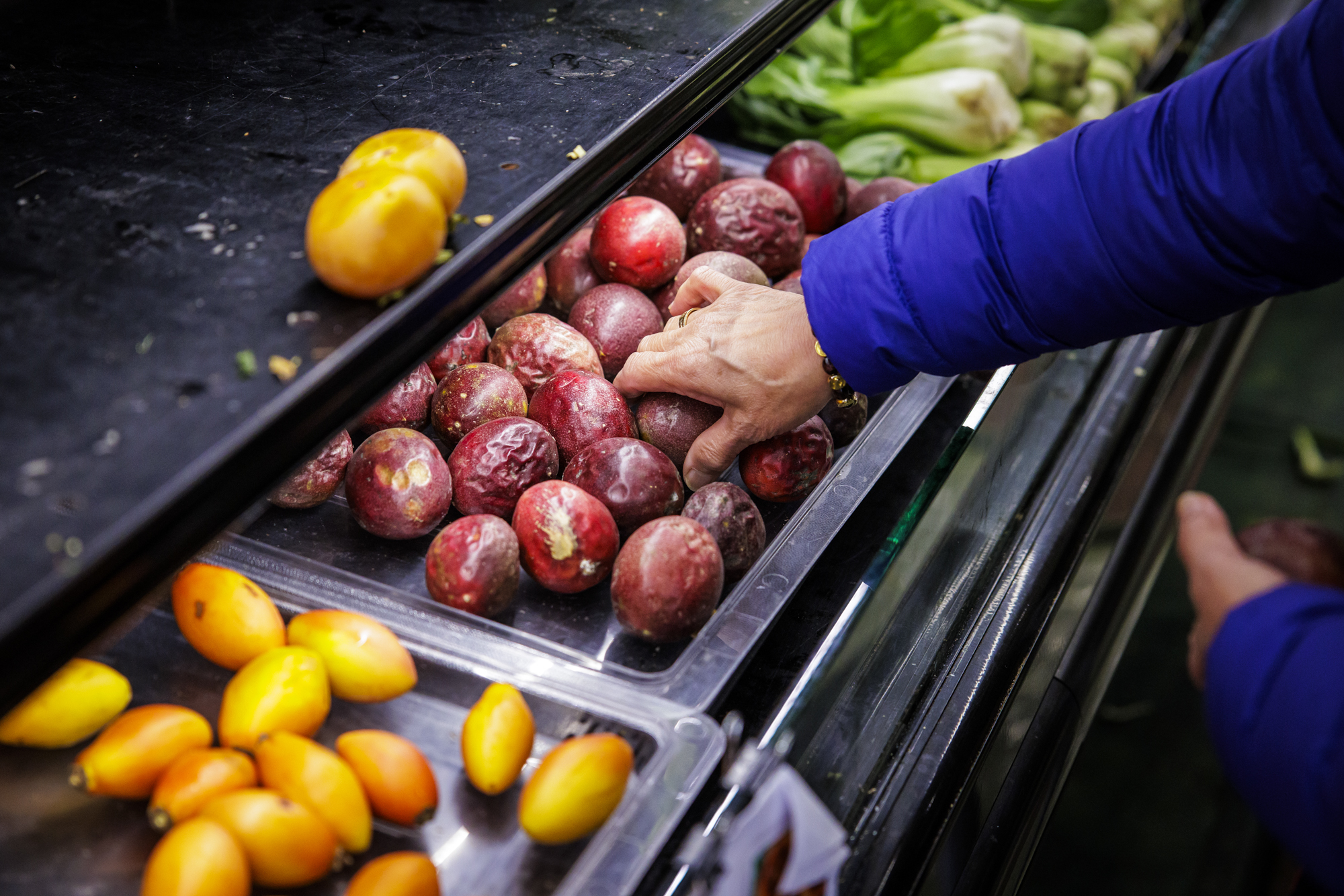 A hand picking up a piece of passion fruit from a produce display.