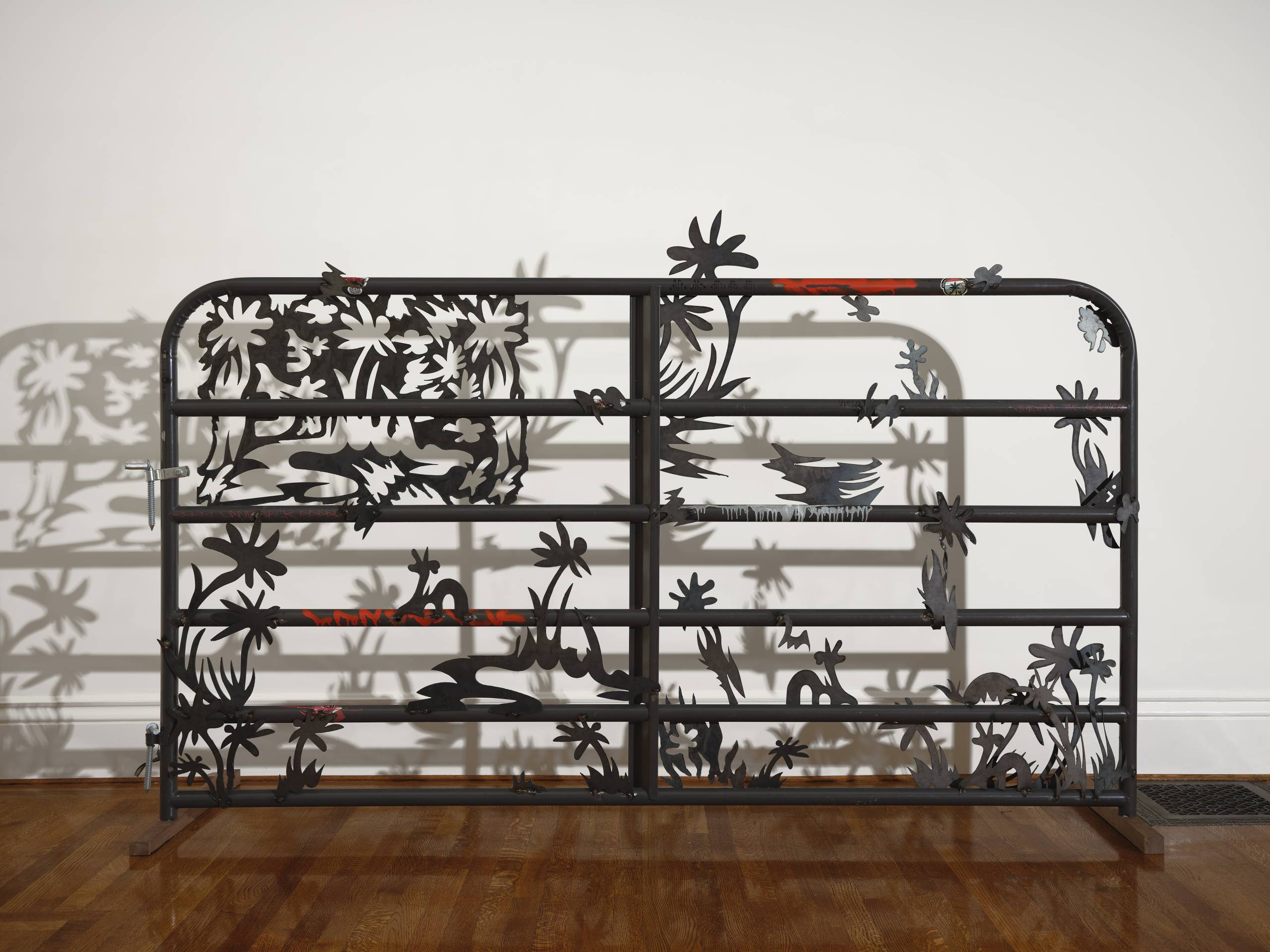 A metal sculpture shaped like a fence with silhouettes of flames and plants.