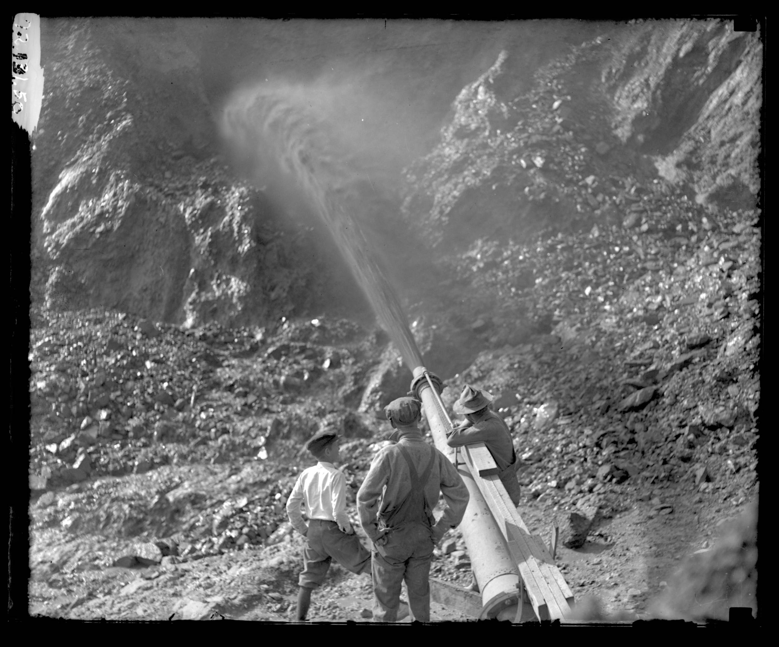 A historical photo of white men blasting a California cliffside with a high-pressure jet of water. 