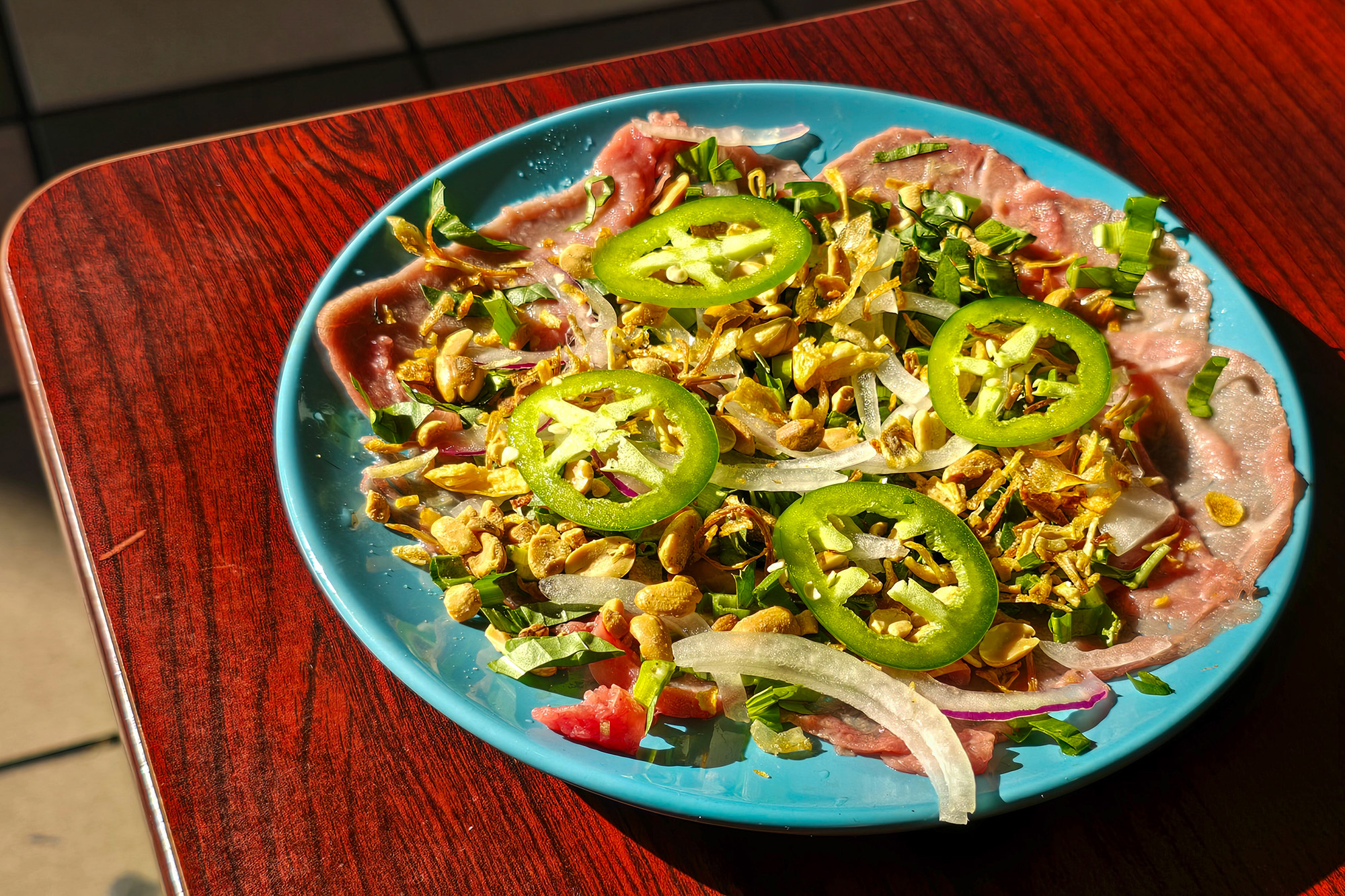 Vietnamese-style beef carpaccio — thin slices of rare beef topped with slices of onion and jalapeño.