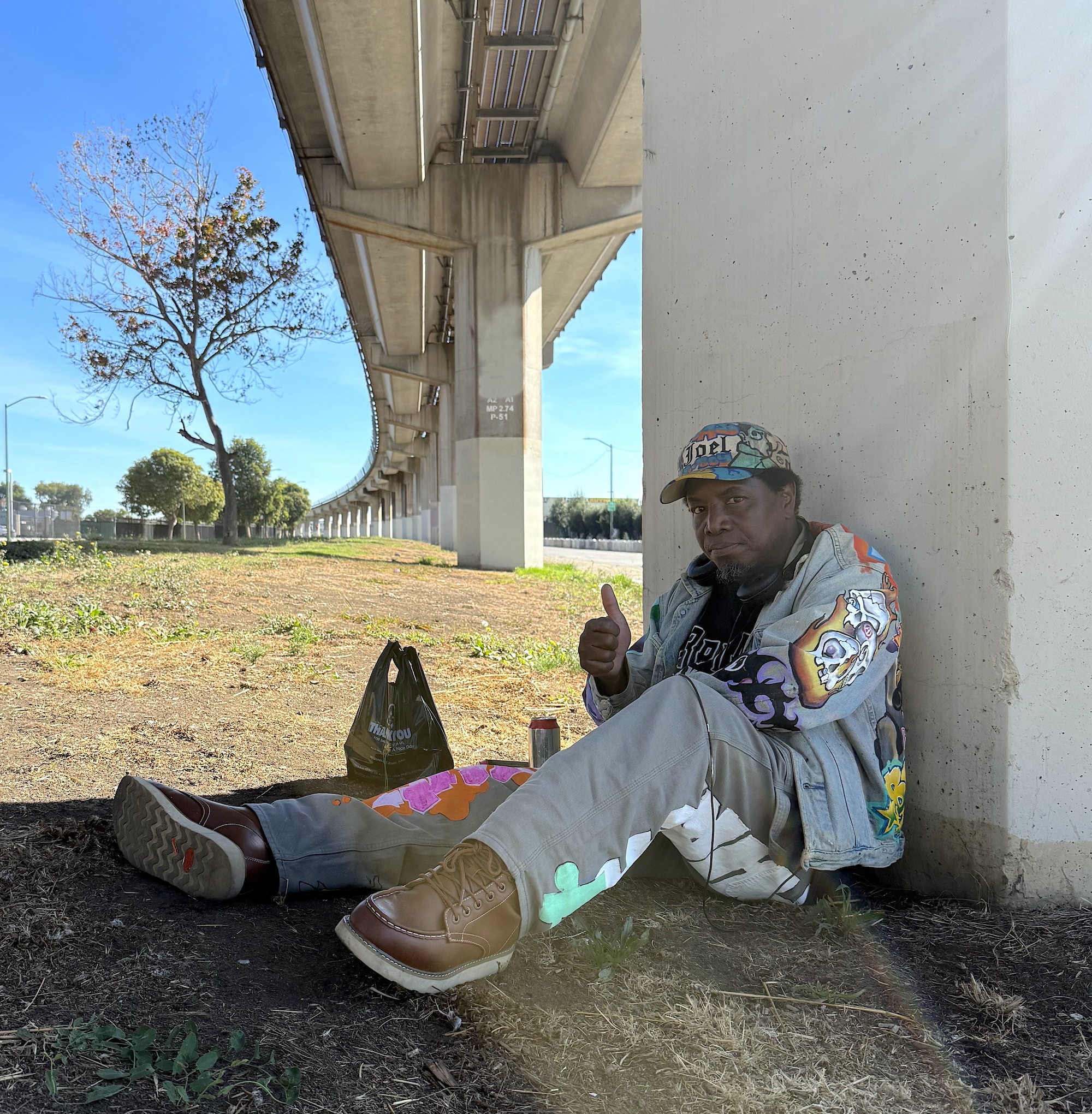 A man in a jean jacket sitting by train tracks.