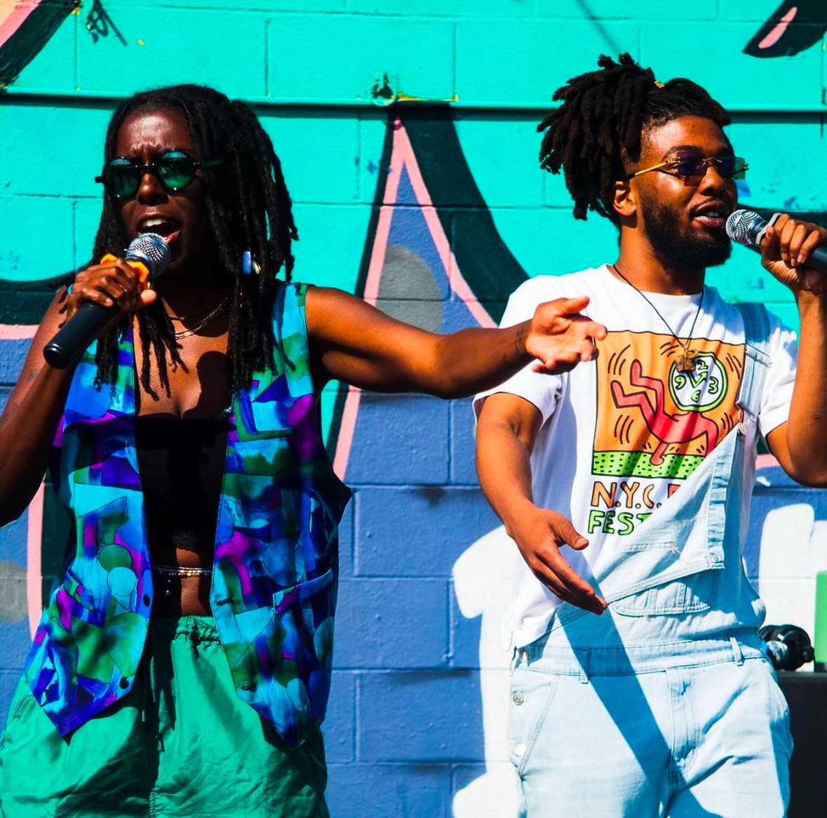 Two rappers on stage wear vibrant, colorful clothing. 