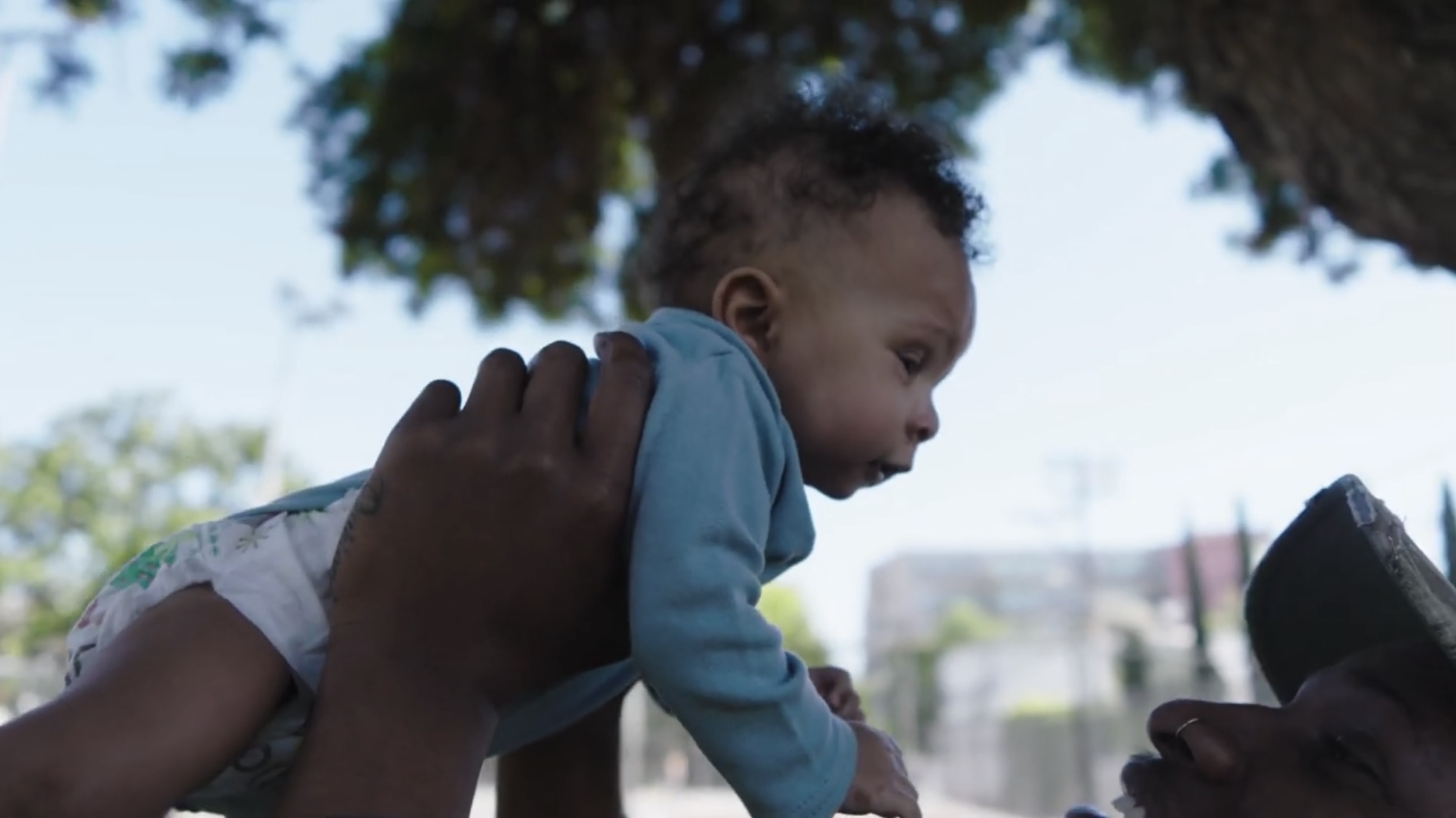 A film still where a young father lifts up an infant.