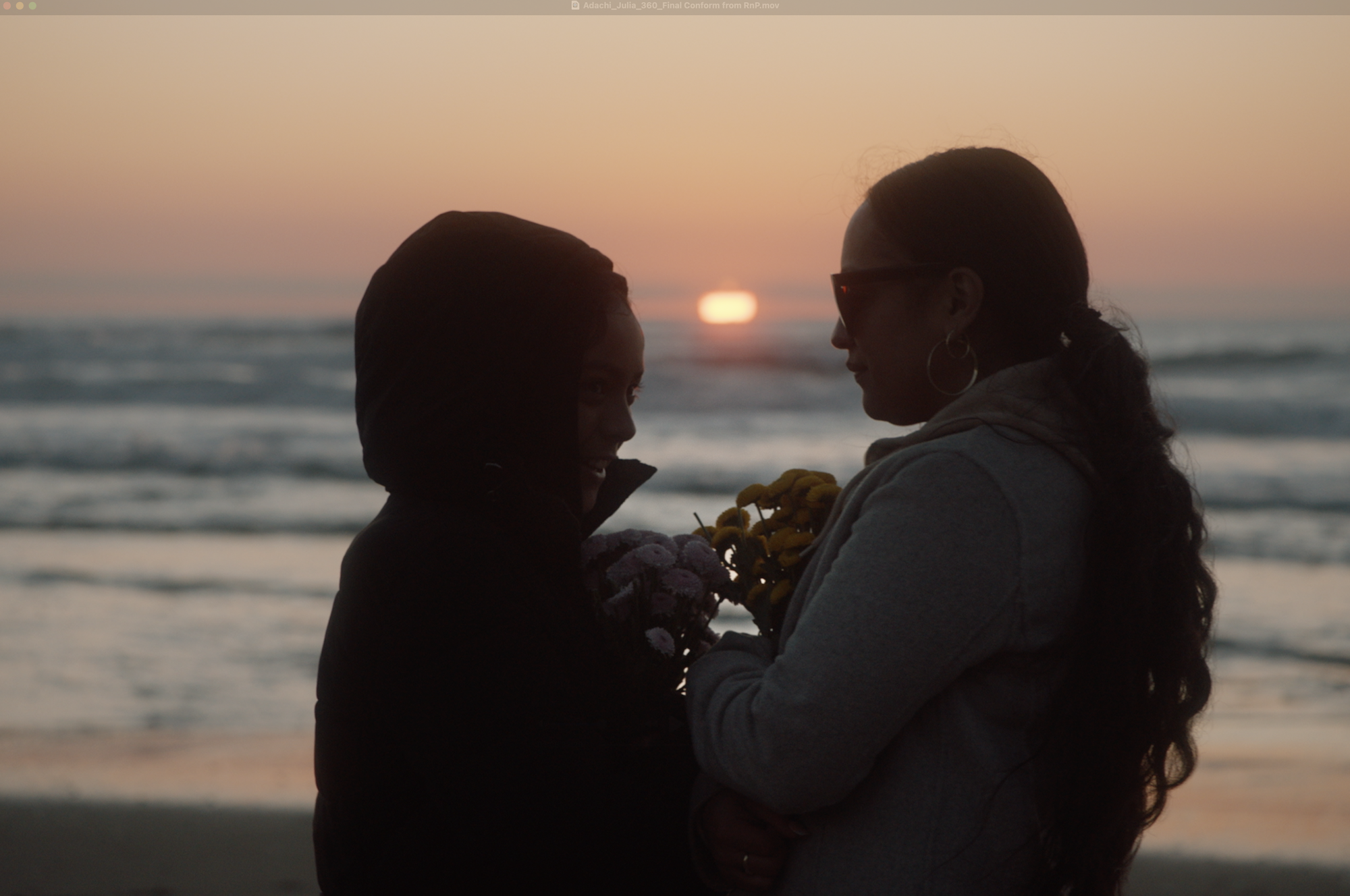 Two women stand on a beach sharing an embrace as the sunsets.