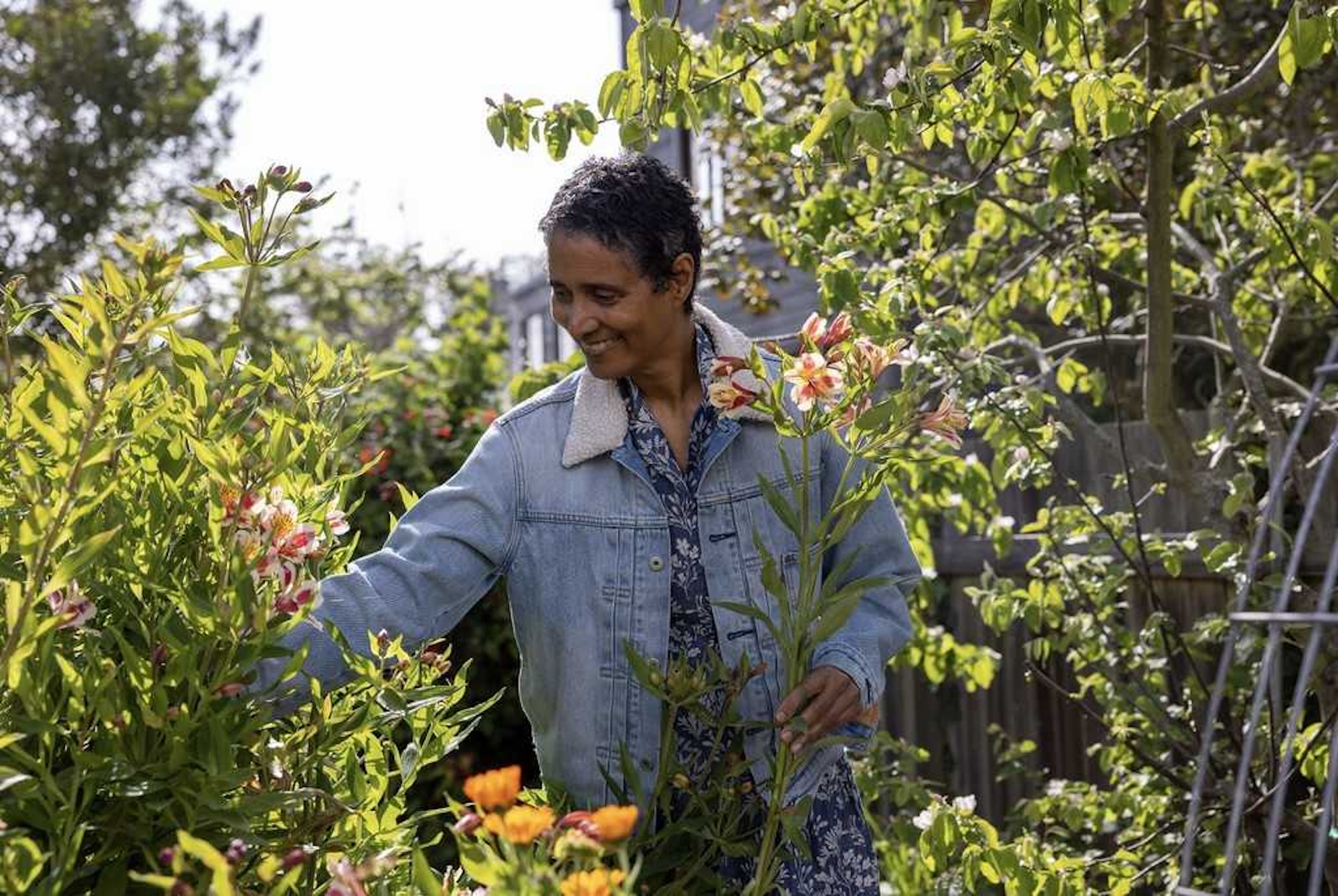 A woman in a jean jacket walking through a garden.