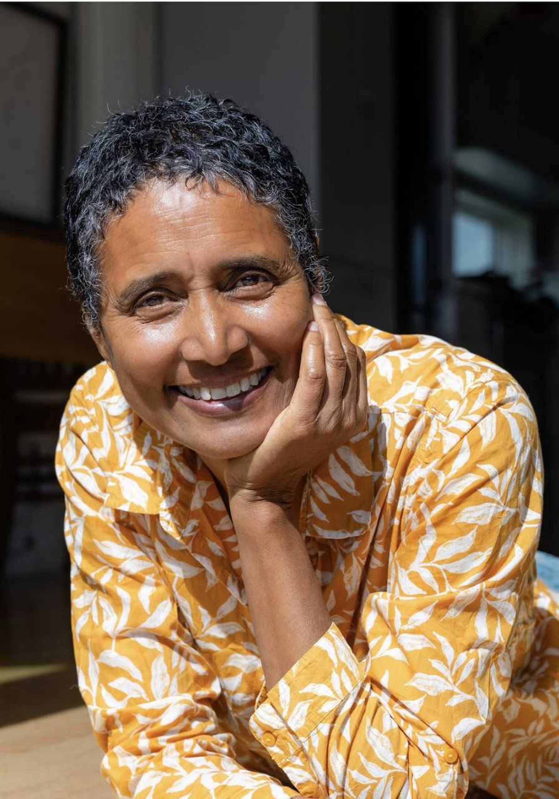 A woman with short hair poses for a photo with her left palm on her chin. 