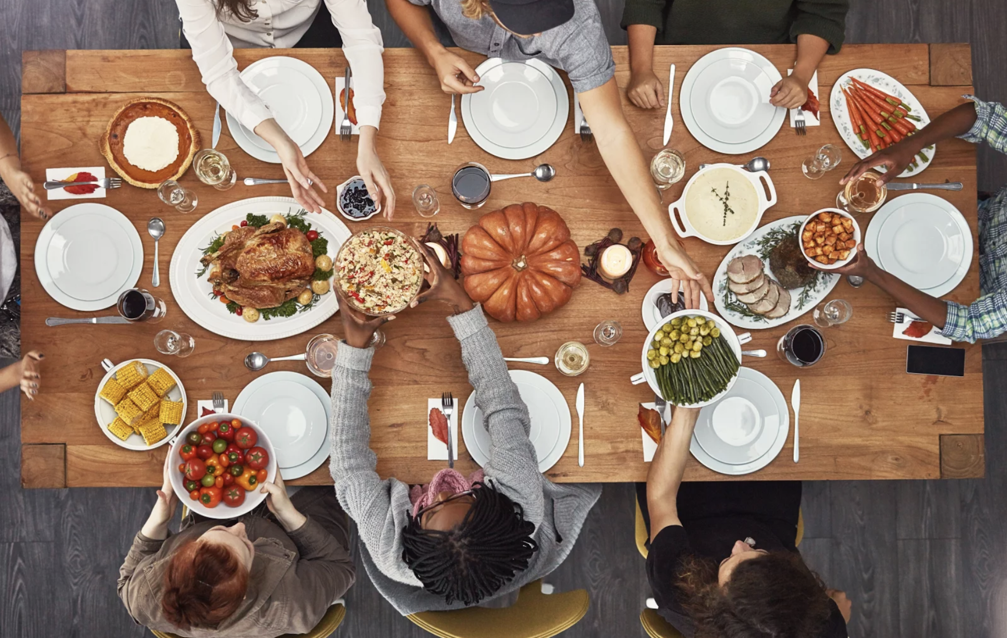 A fall-season dinner table viewed from above with six people sharing dishes. A pumpkin sits at the center of the table.