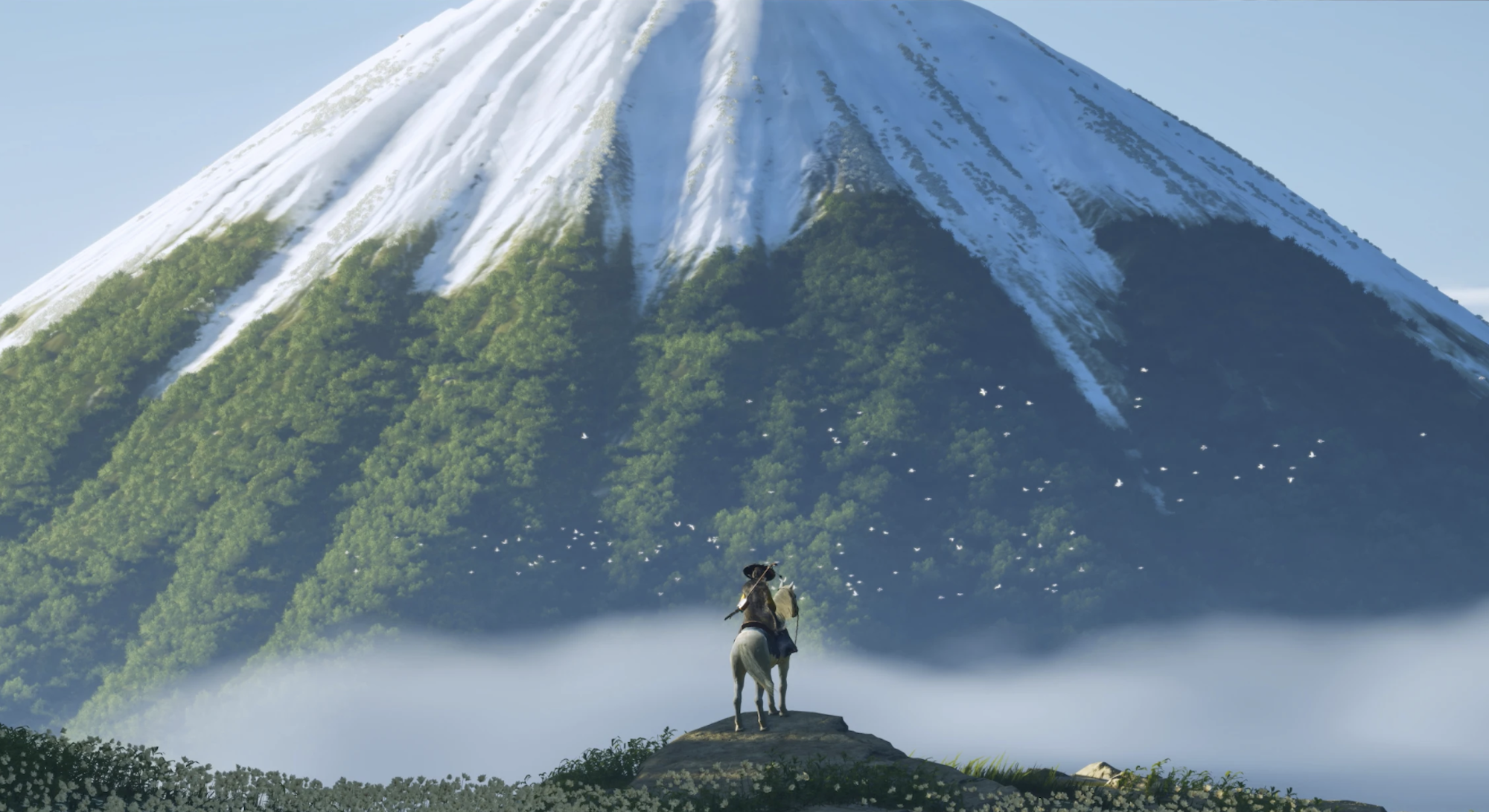 A lone figure on a horse stands in the shadow of an enormous snow-capped mountain.