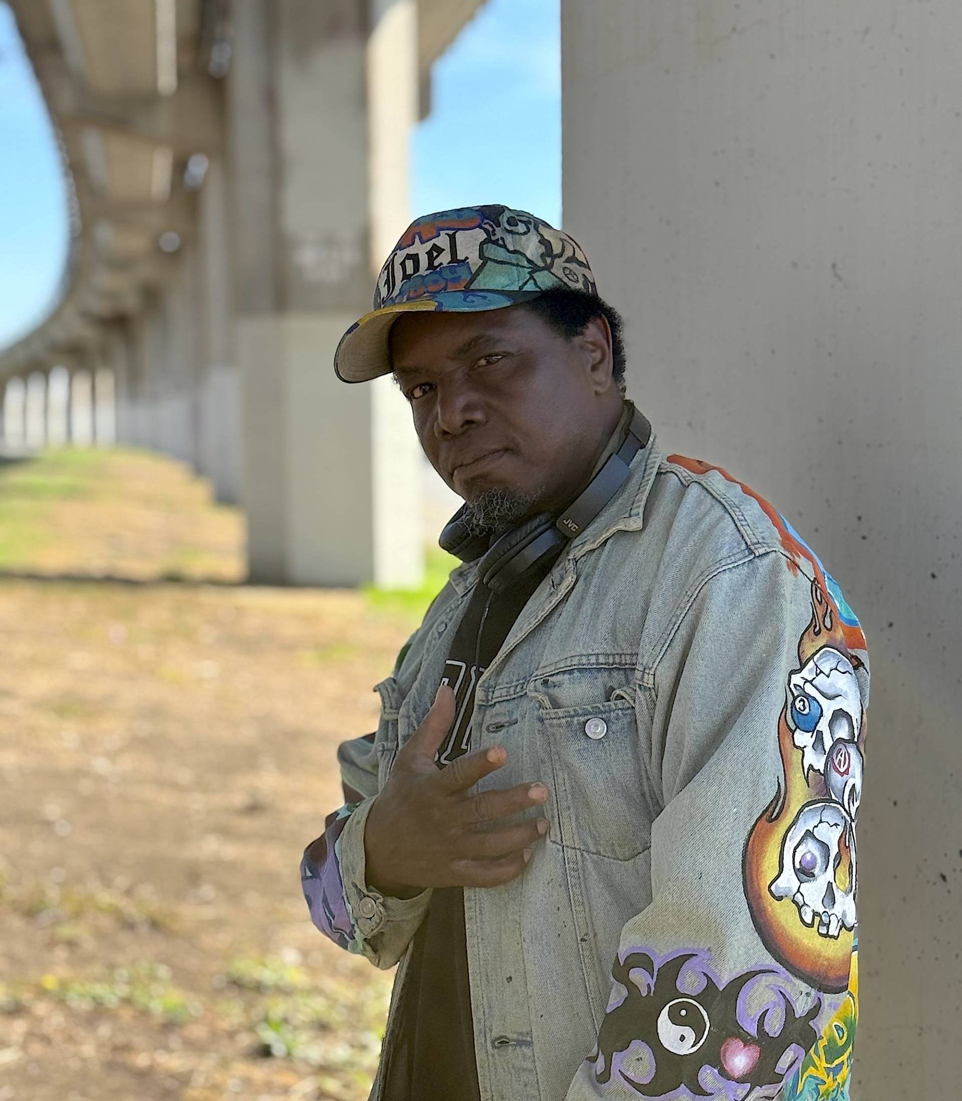 An African American man in a colorful hat and painted jean jacket.