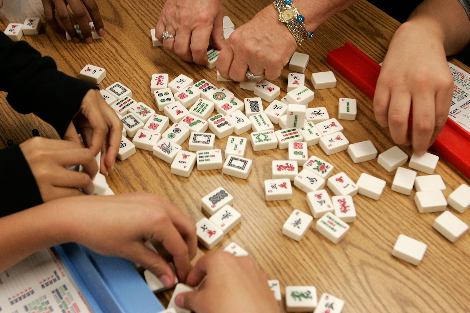Four sets of hands work around a table to flip over a set of colorful mahjong tiles.
