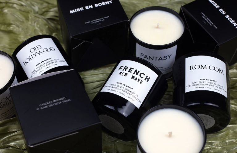 White candles in black jars lay randomly arranged on a green velvet blanket.