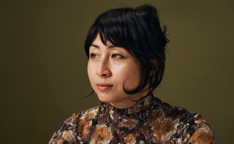 A well-presented middle-aged Asian woman sits in traditional portrait pose, wearing a brown and rust colored floral, mock neck top.