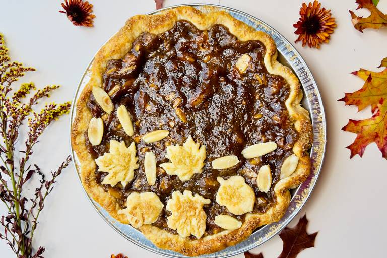Overhead shot of a festive holiday pie with a glistening brown filling, topped with pieces of dough shaped like maple leaves.