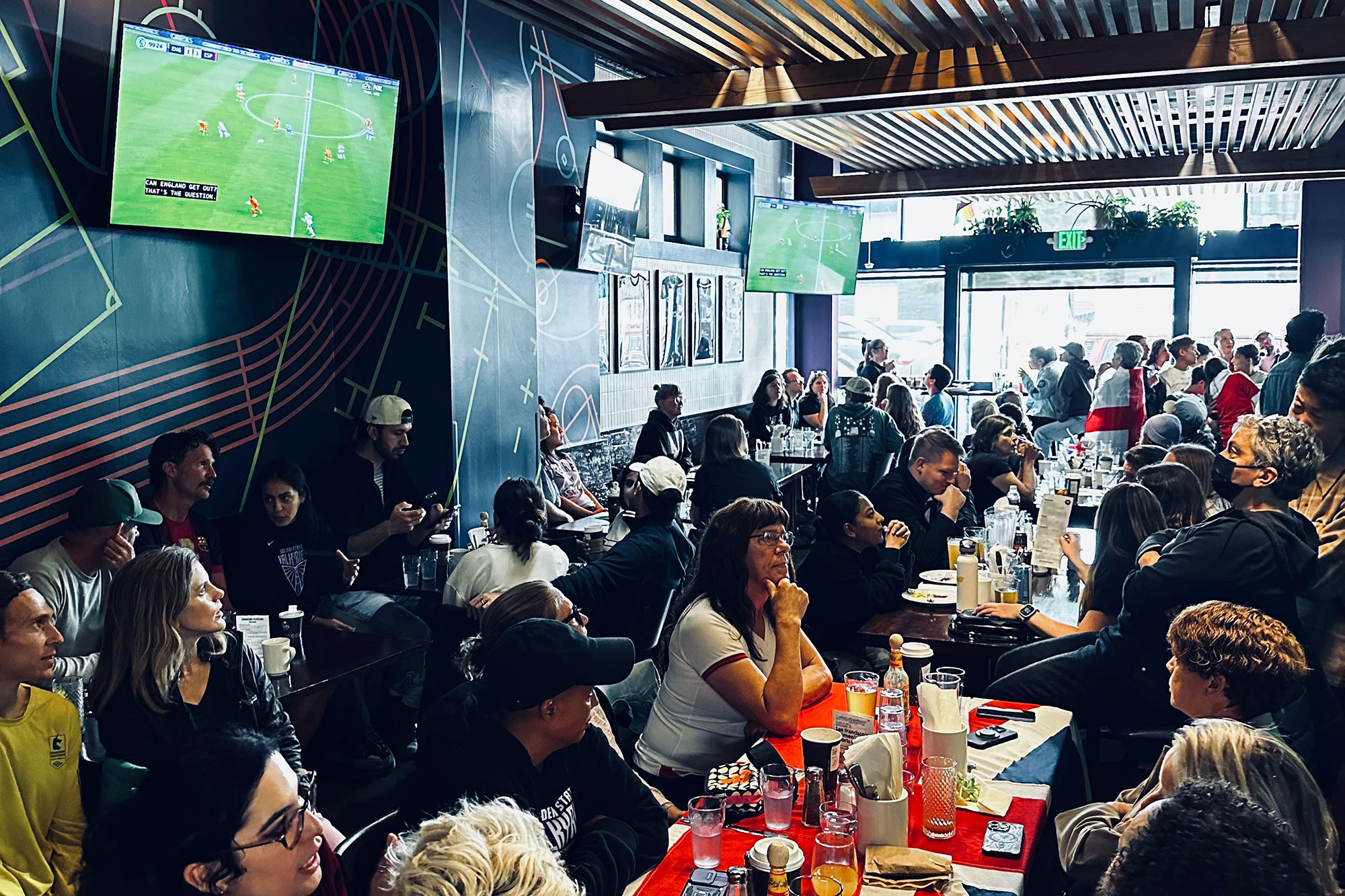 A soccer match being shown on the TVs in a crowded sports bar.