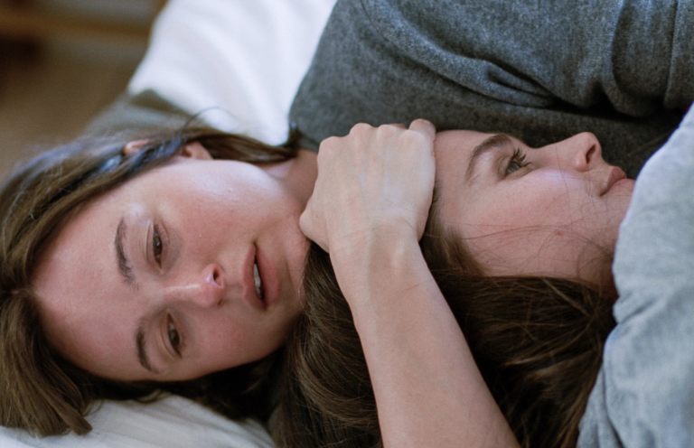 A distressed and crying white woman lies down, clutching another woman's head close to her chest.