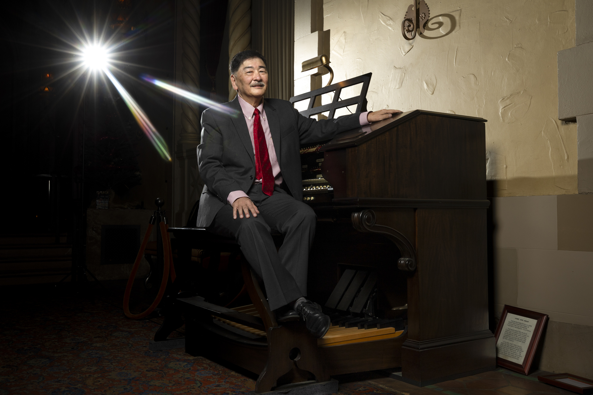 An organ player in a suit sits at his instrument in a dark theater.
