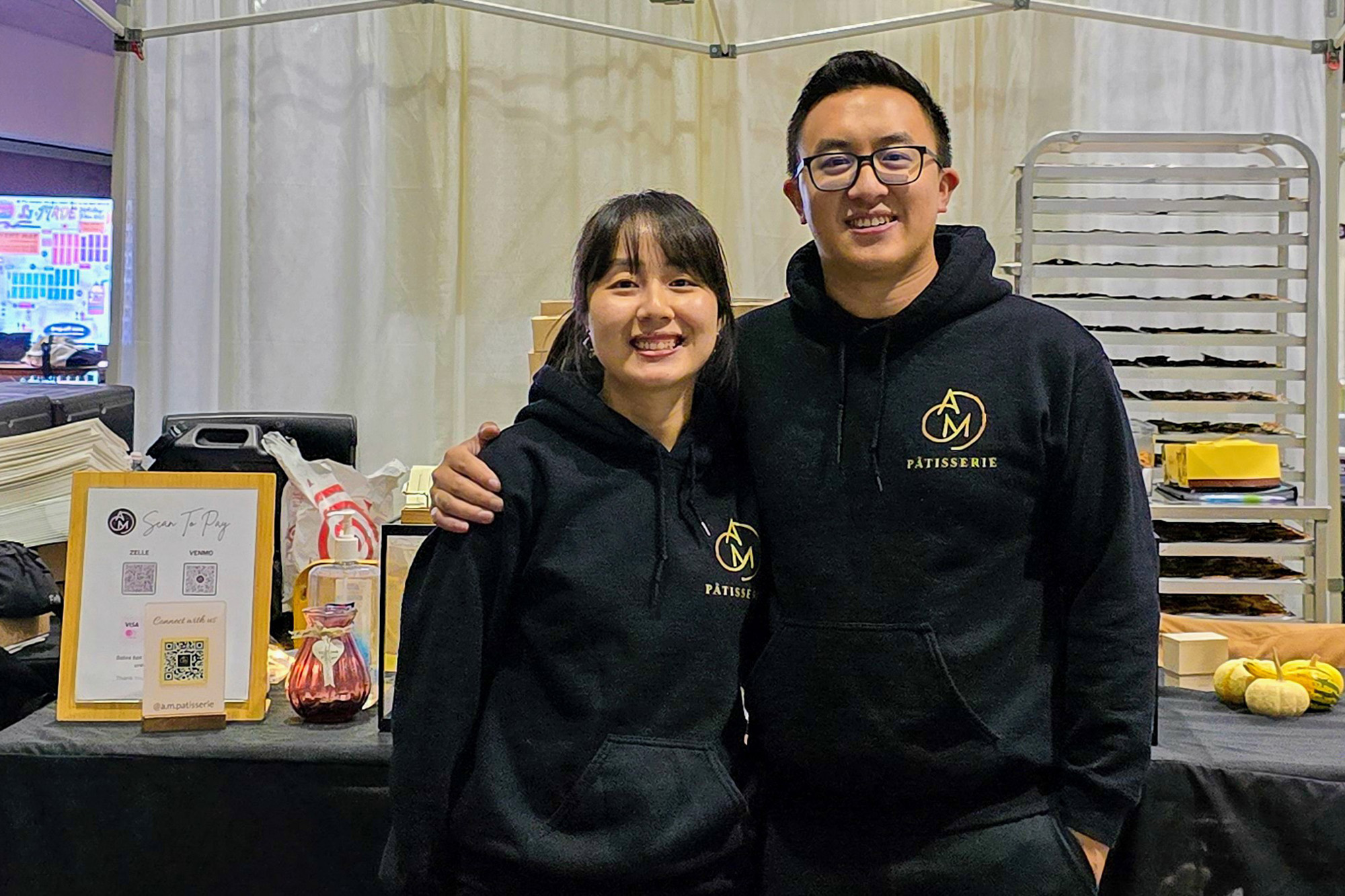 An Asian woman and man in matching black hooded sweatshirts.