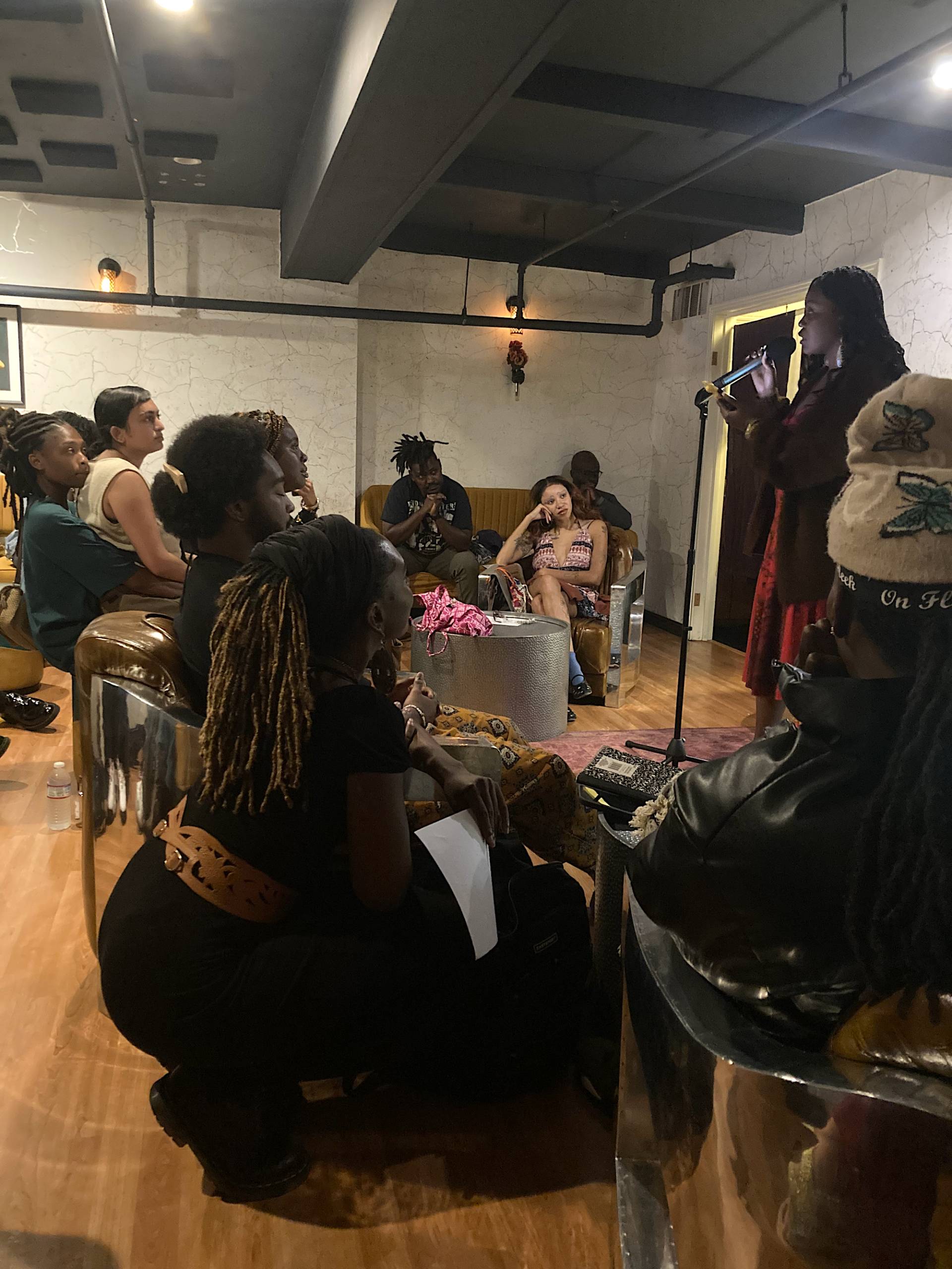 A woman kneels in the crowd as a performer recites a poem on stage during a live performance event. 