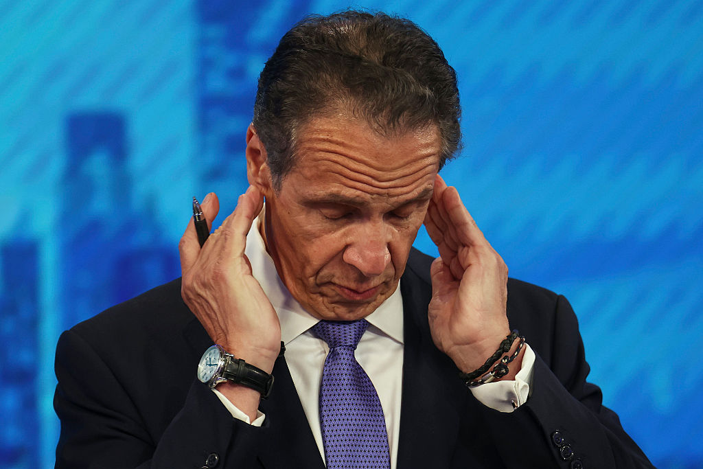 A politician in a suit rubs his temples with a stressed-out expression. 