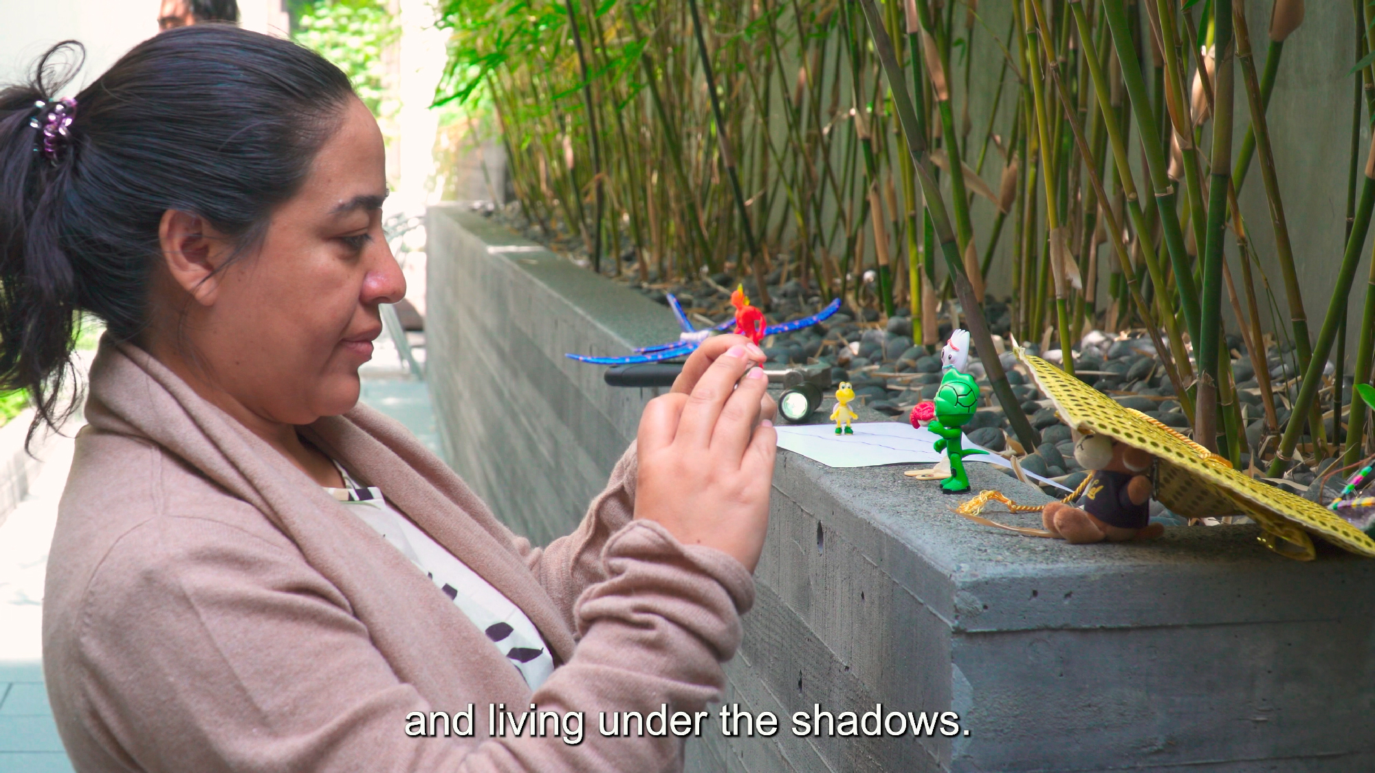person holds phone up while creating video using small toys, subtitle reads 'and living under the shadows.'