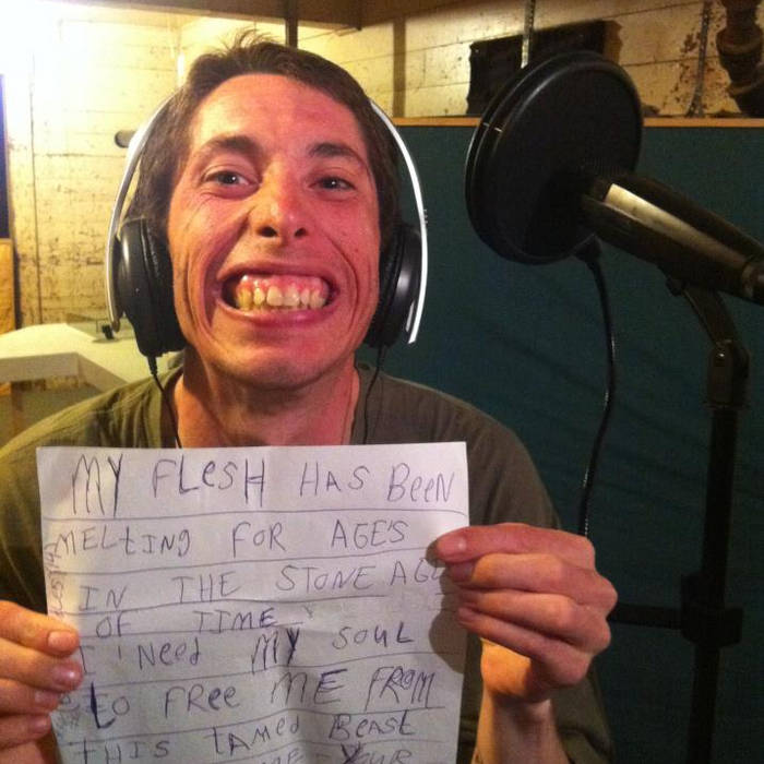 A young man wearing headphones looks into the camera and smiles while holding piece of paper with lyrics on it