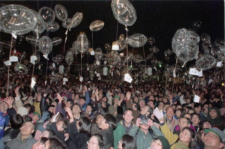 large crowd at night with paper in clear balloons above