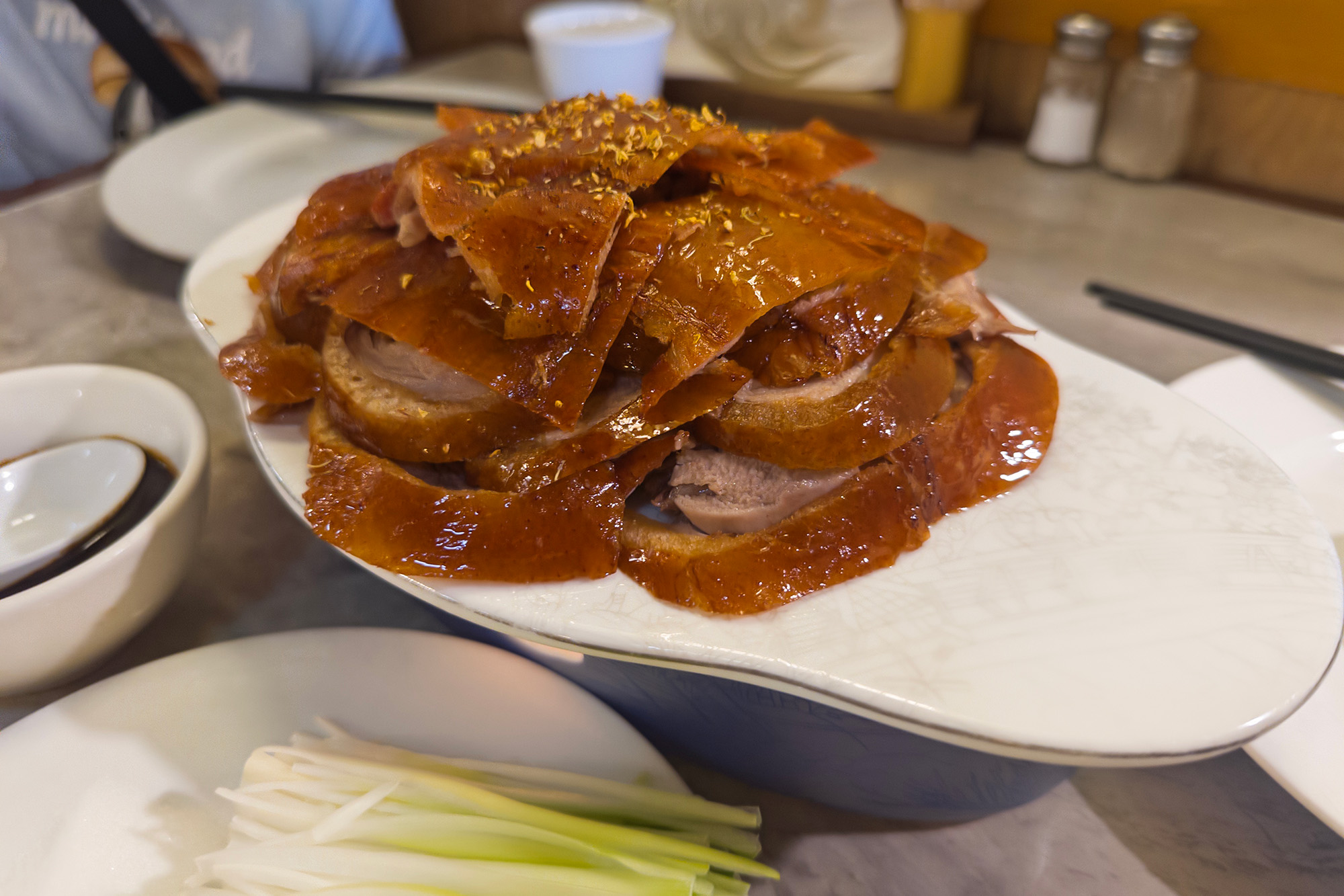 Peking duck with golden-brown skin, sliced up and arranged on a platter.