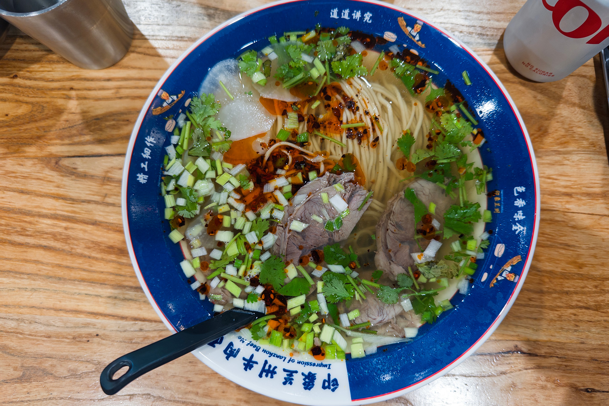 Overhead view of a bowl of clear beef noodle soup topped with a scattering of chopped cilantro and garlic shoots.