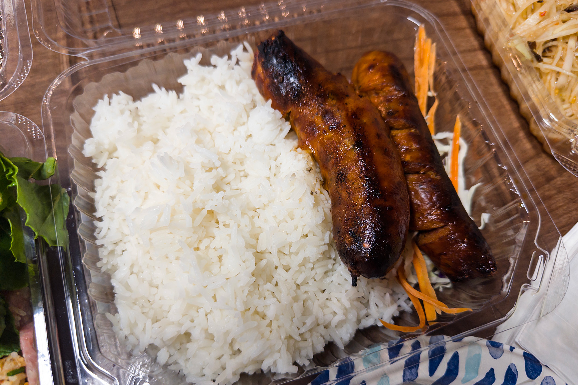 Two charred sausages served with white rice in a plastic takeout container.
