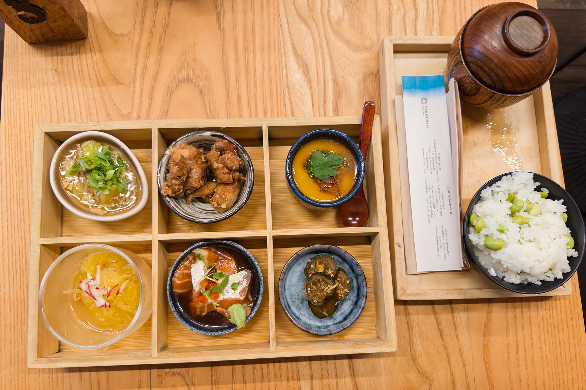 A set Japanese meal, served in a partitioned wooden box, with rice and soup on the side.
