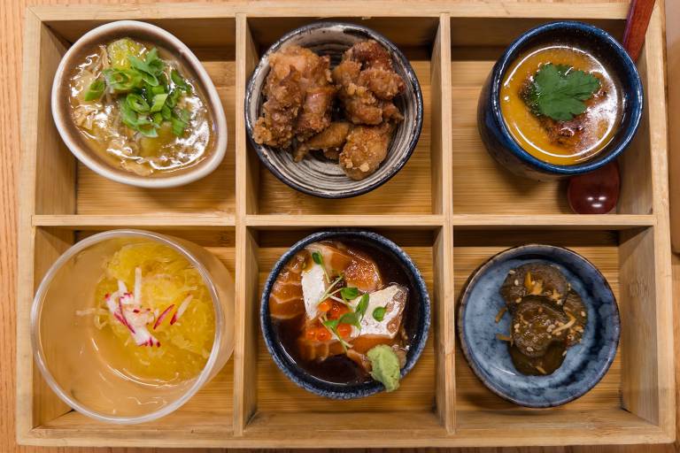 Overhead view of six elegant Japanese dishes served in a partitioned wooded box.