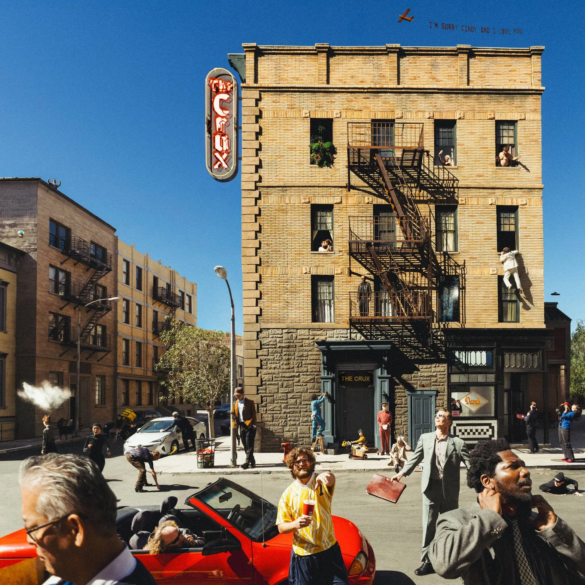 a four-story brick building with various scenes in its windows stands in front of a street with cars and people