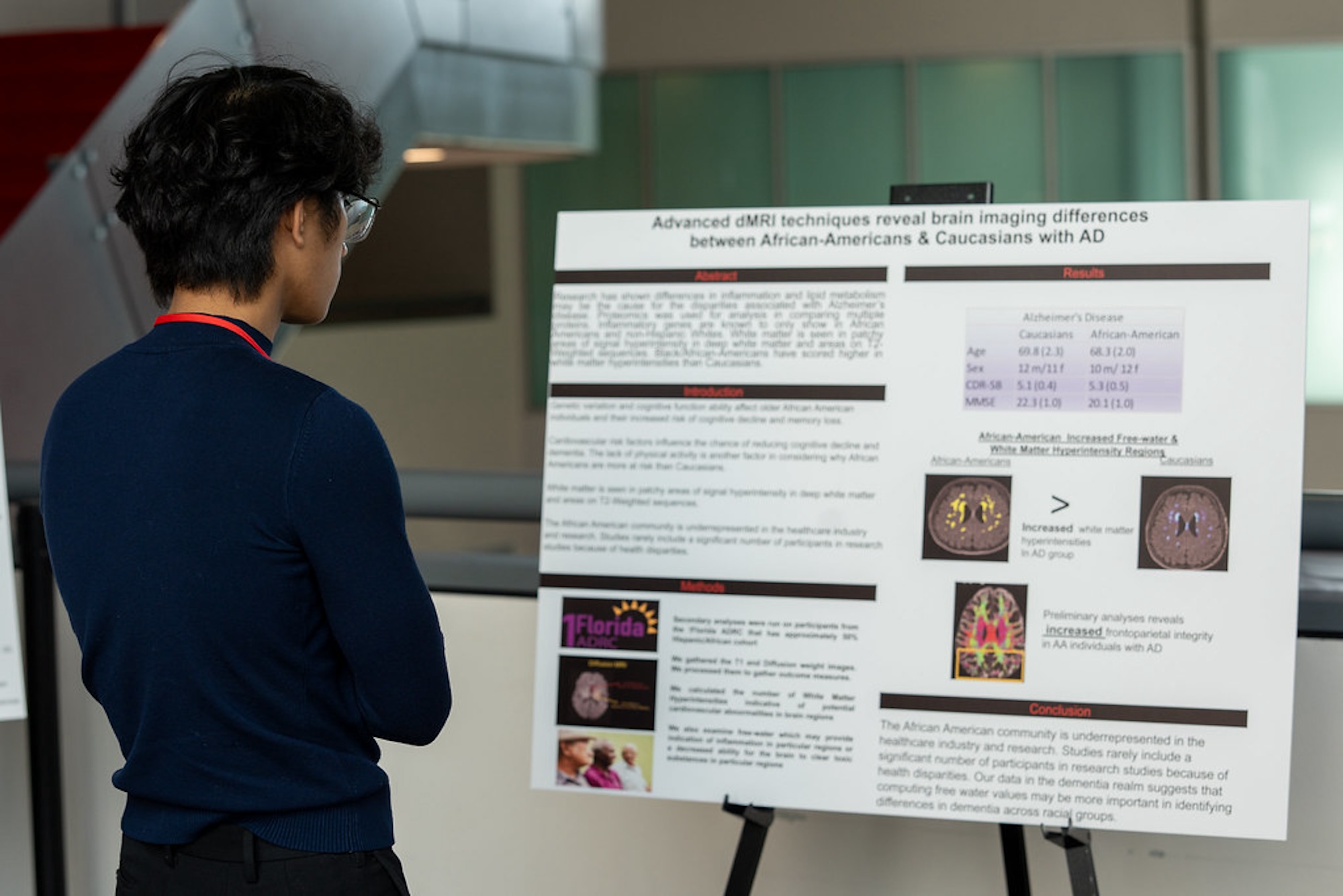 A person in a blue shirt stands as they read a sign with information regarding health outcomes for Black men in America. 