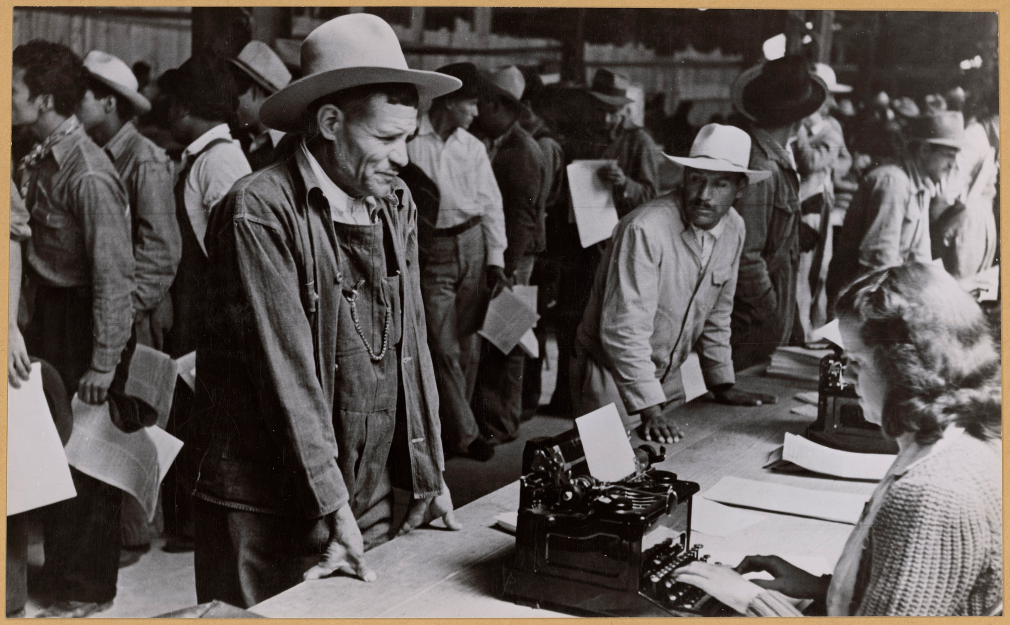 men in workwear and cowboy hats in front of long table with people registering paperwork