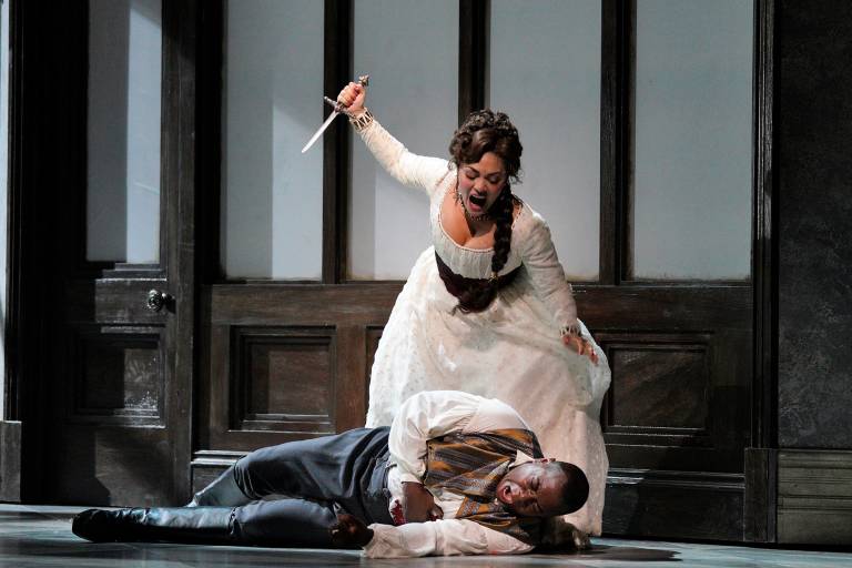 A woman in white hoists a dagger above a man laying on the ground