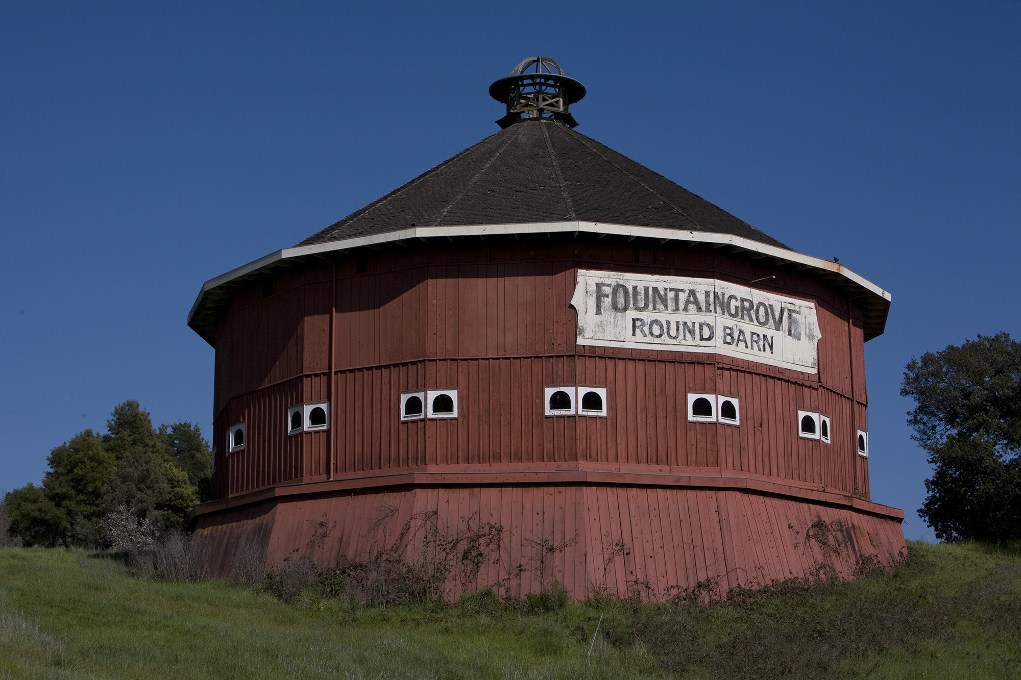 A large red barn sits atop a small hill of green grass, with blue sky in the background