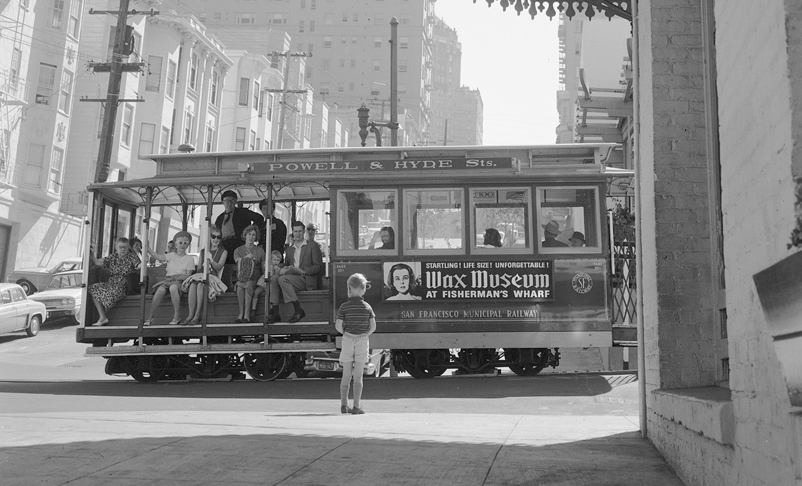 black-and-white image of small chid in front of cable car with passengers